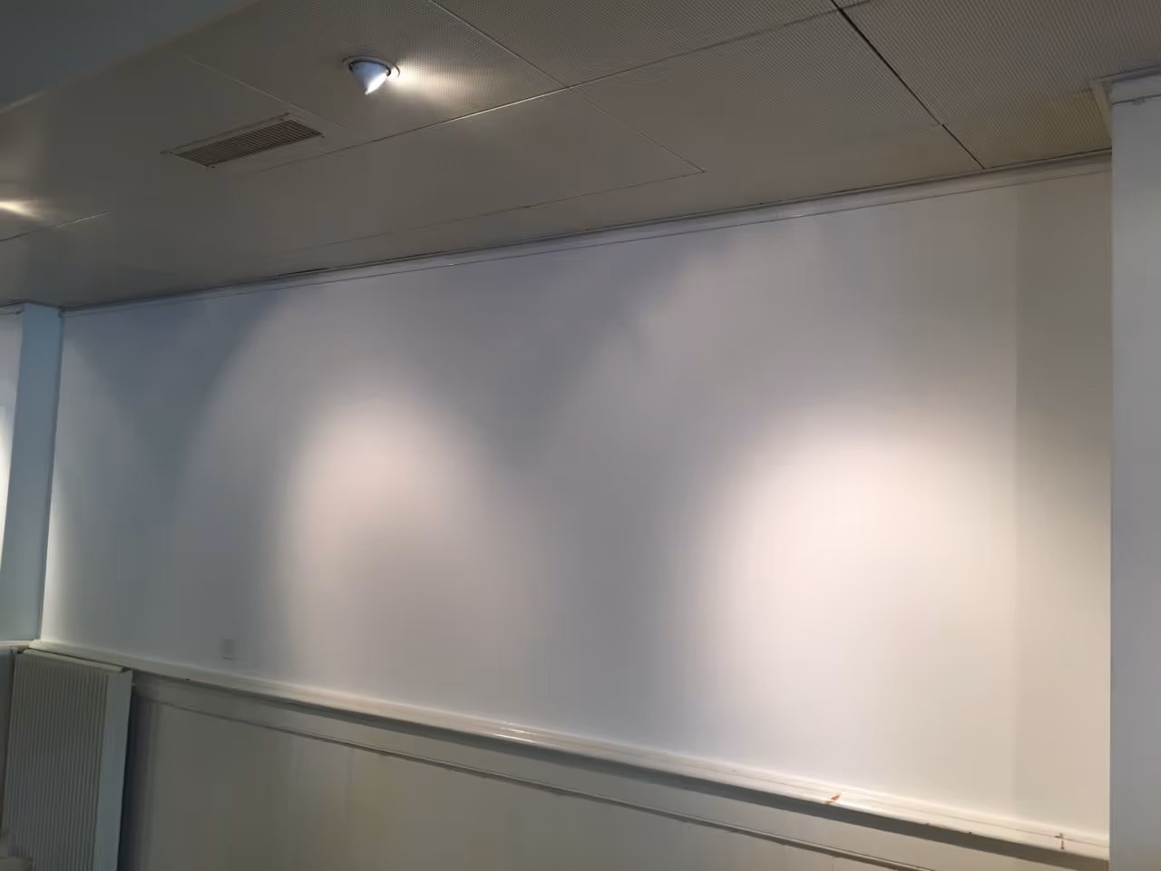 Leere weiße Wand in einem Raum mit Deckenbeleuchtung und einem Heizkörper an der Wand.