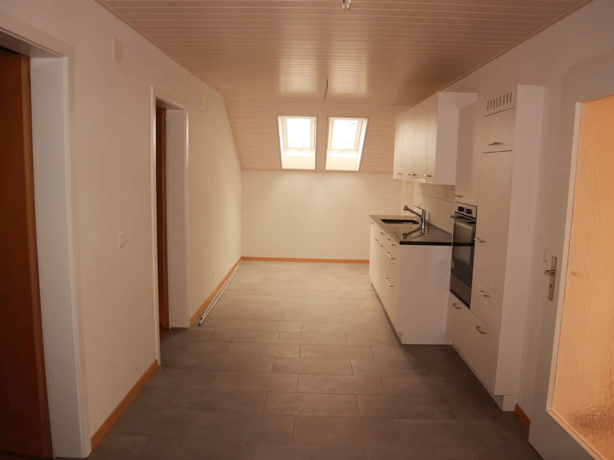 Kleine moderne Küche mit weissen Schränken, schwarzen Arbeitsplatten und zwei Dachfenstern im Dachgeschoss.