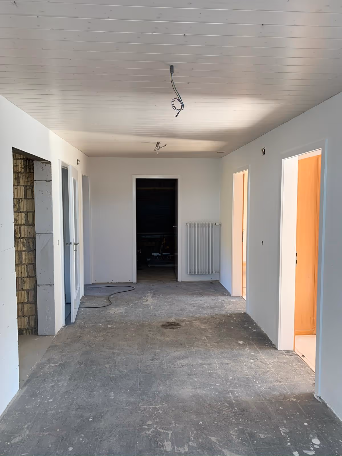Innenraum eines Hauses während der Renovierung mit unverputzten Böden, weißen Wänden und mehreren offenen Türen.