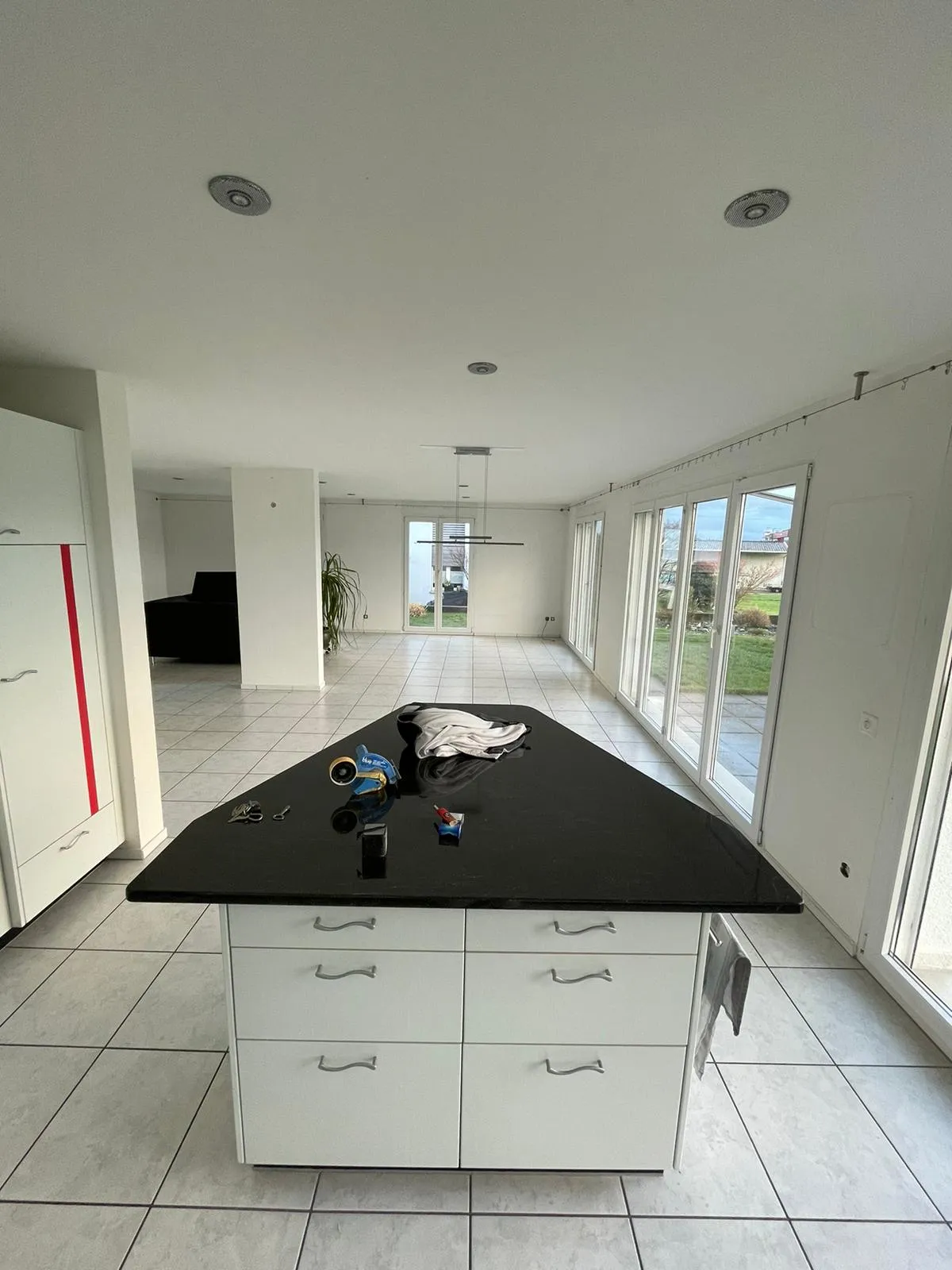 Moderner, leerer Wohnraum mit weißen Fliesen und Kücheninsel mit schwarzer Arbeitsplatte und einigen Gegenständen darauf.