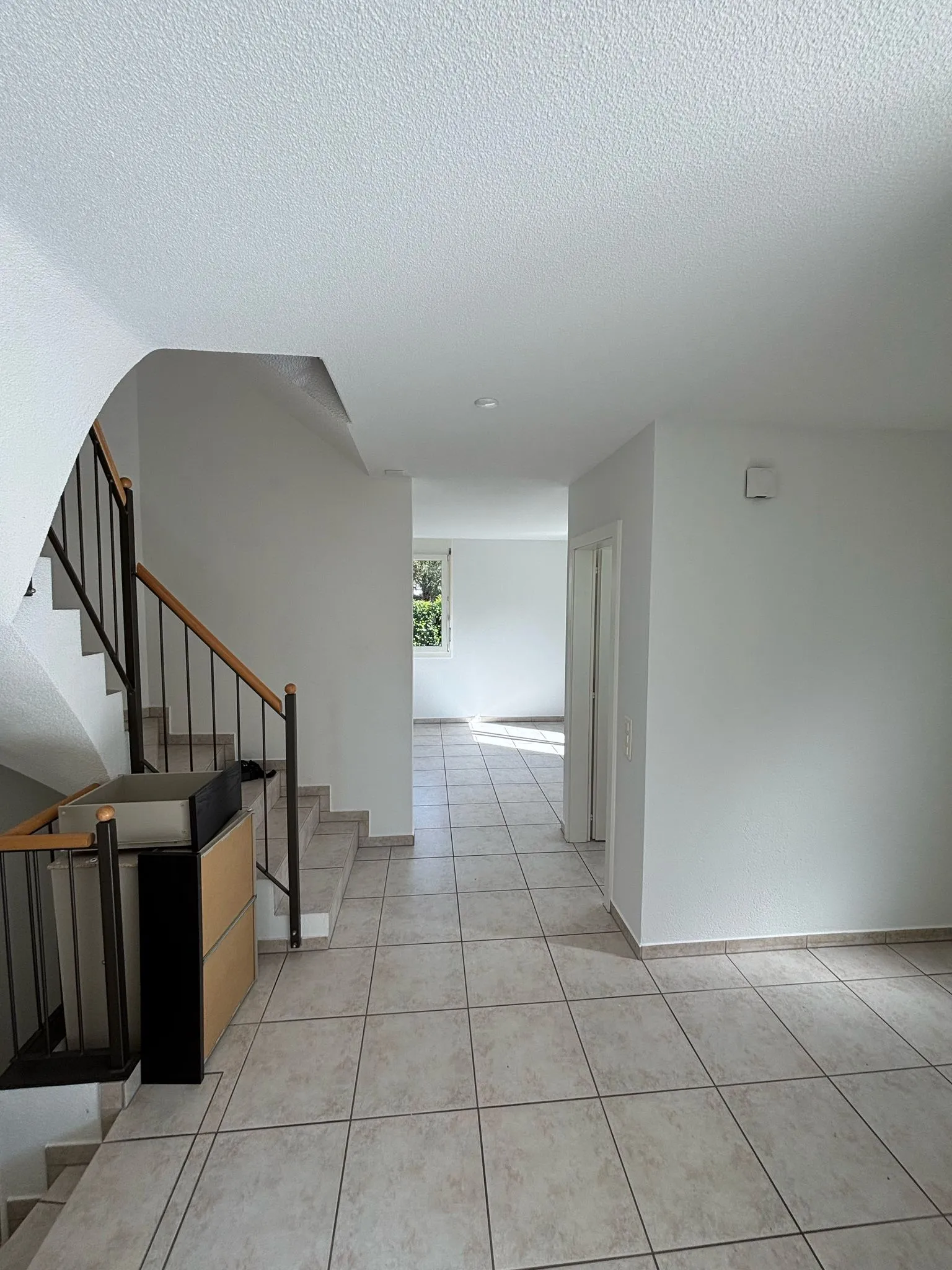 Helle Wohnung mit beigen Fliesenboden, Treppe mit Holzhandlauf und weißen Wänden.