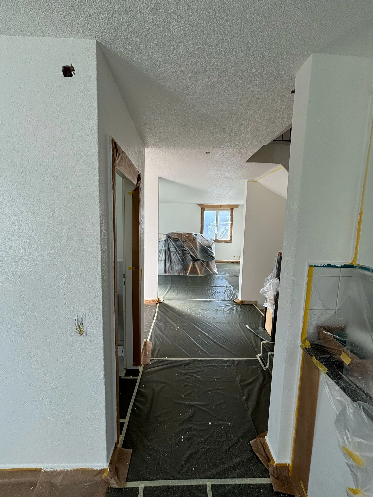 Innenraum eines Hauses mit frisch gestrichenen weißen Wänden und Schutzabdeckungen auf dem Boden und Möbeln.