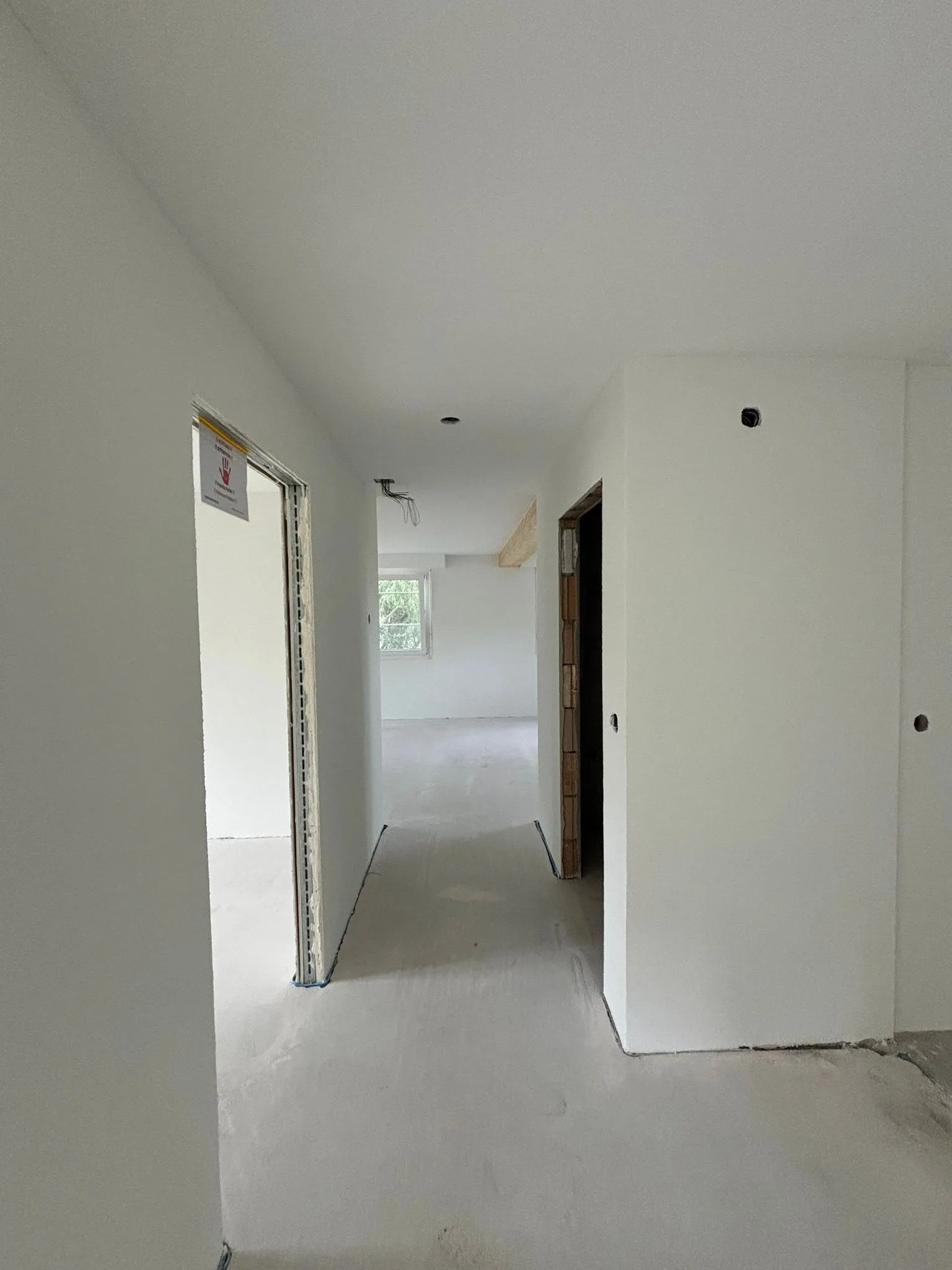 Korridor in einem Rohbau mit unvollendeten Türen und weiß gestrichenen Wänden.
