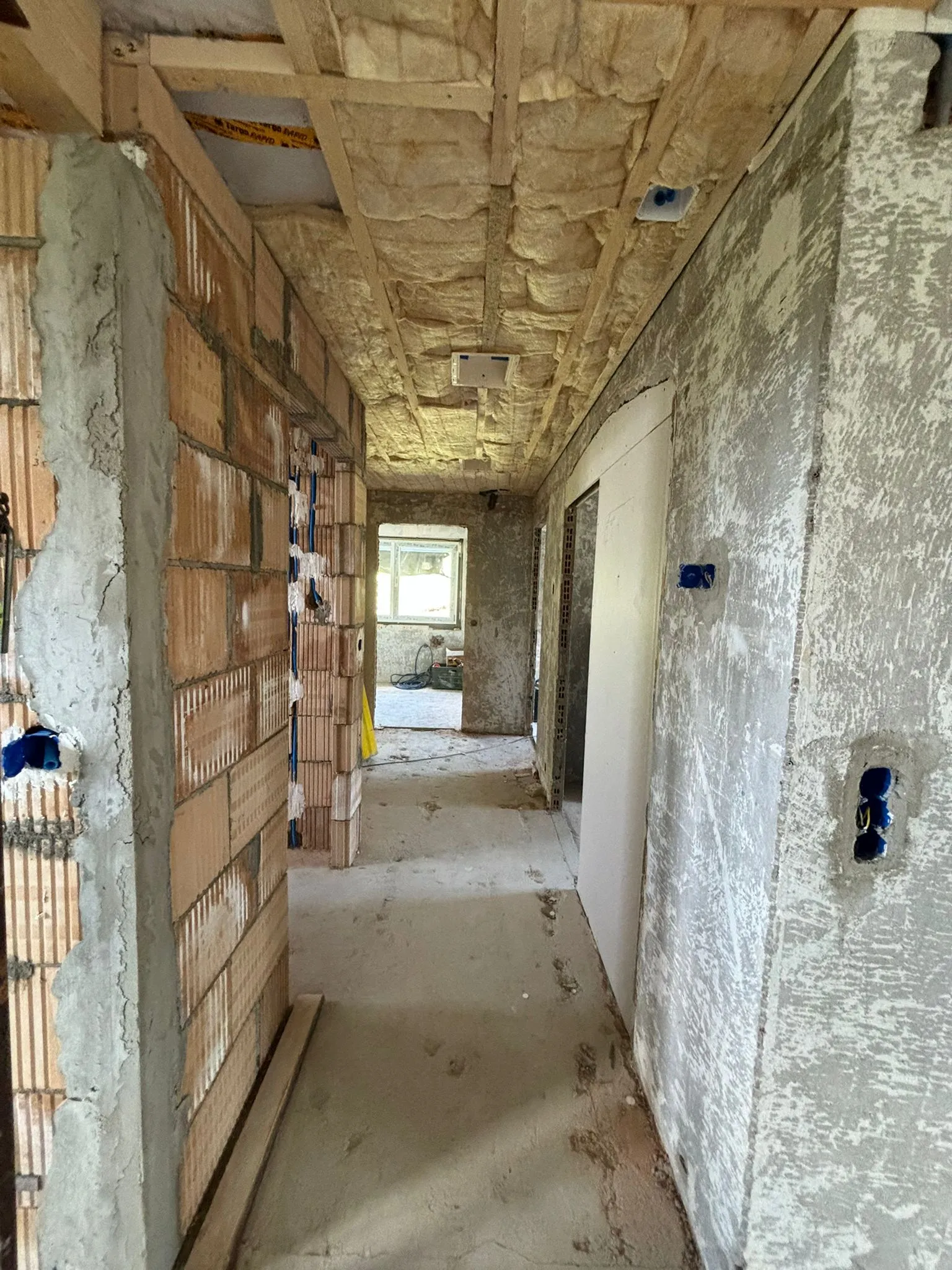 Flur in einem Rohbau mit unverputzten Wänden, sichtbaren Ziegelsteinen und gedämmter Decke.