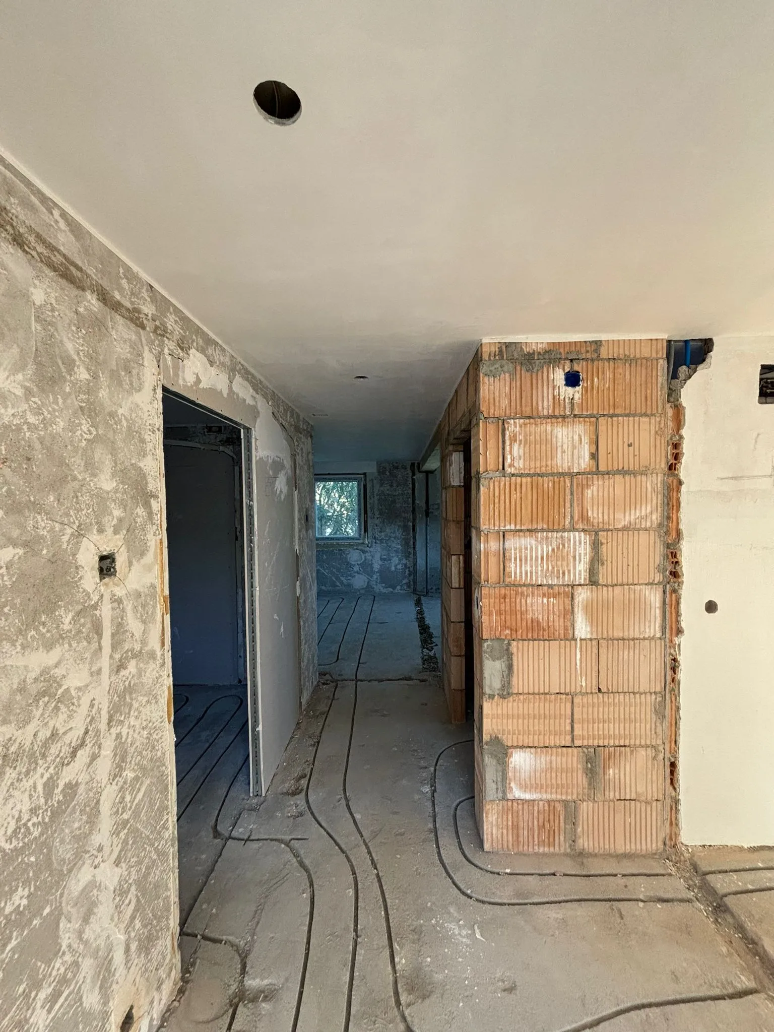 Unrenovierter Flur mit sichtbaren Kabelschächten im Betonboden und unverputzten Ziegelwänden.
