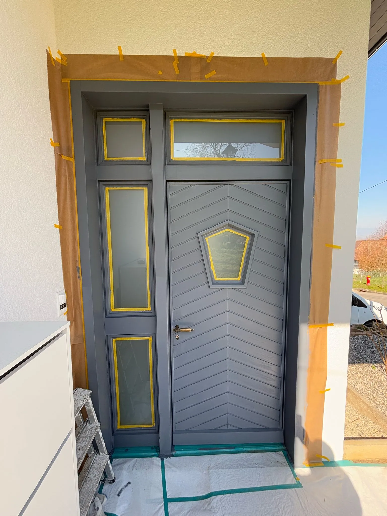 Eingangstür mit Fenster und Rahmen, die für Anstricharbeiten abgeklebt sind.