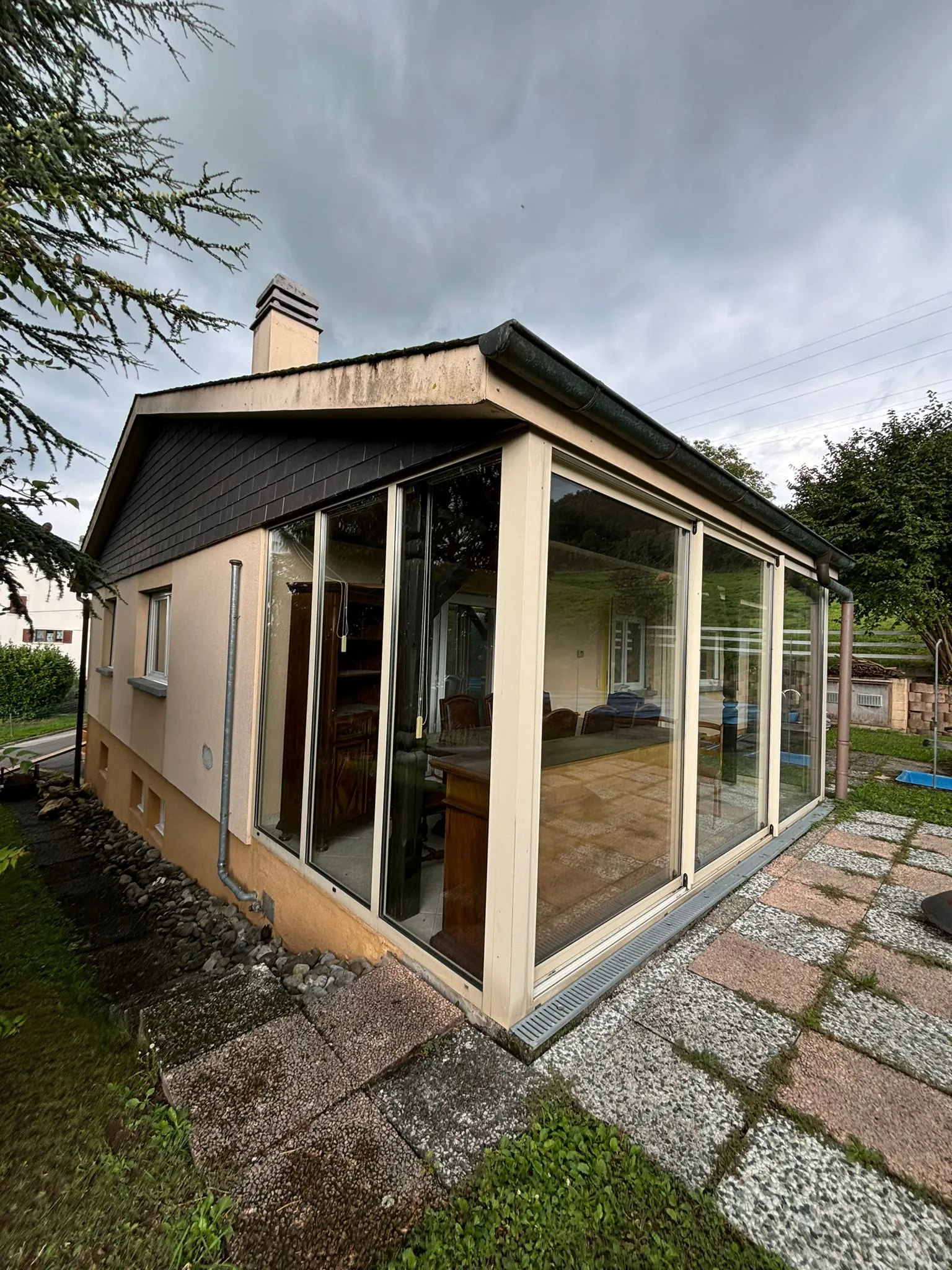 Einfamilienhaus mit Glasanbau und gepflastertem Weg bei bewölktem Himmel.