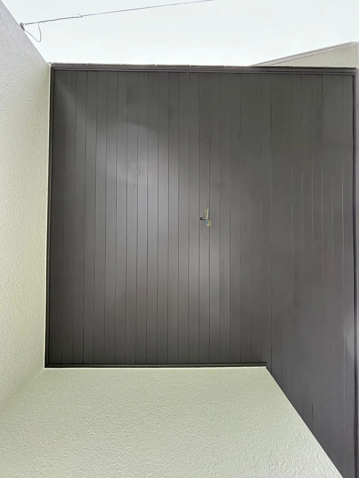 Dunkle, vertikal gestreifte Decke in einem aufrechten, viereckigen Raum mit hellen, strukturierten Wänden und einem kleinen Haken in der Mitte.