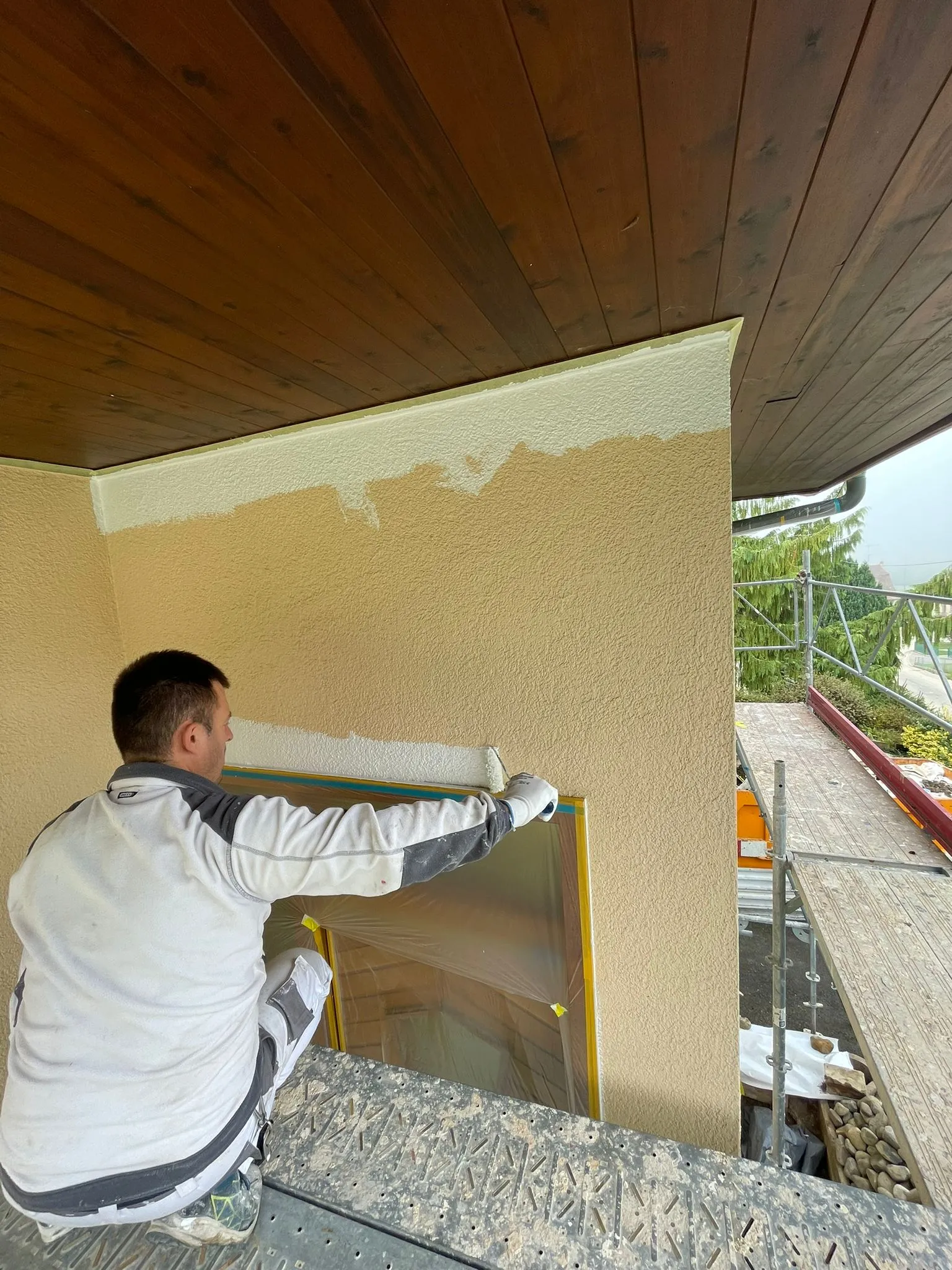 Mann streicht eine Aussenwand eines Hauses in Weiss auf einem Gerüst.