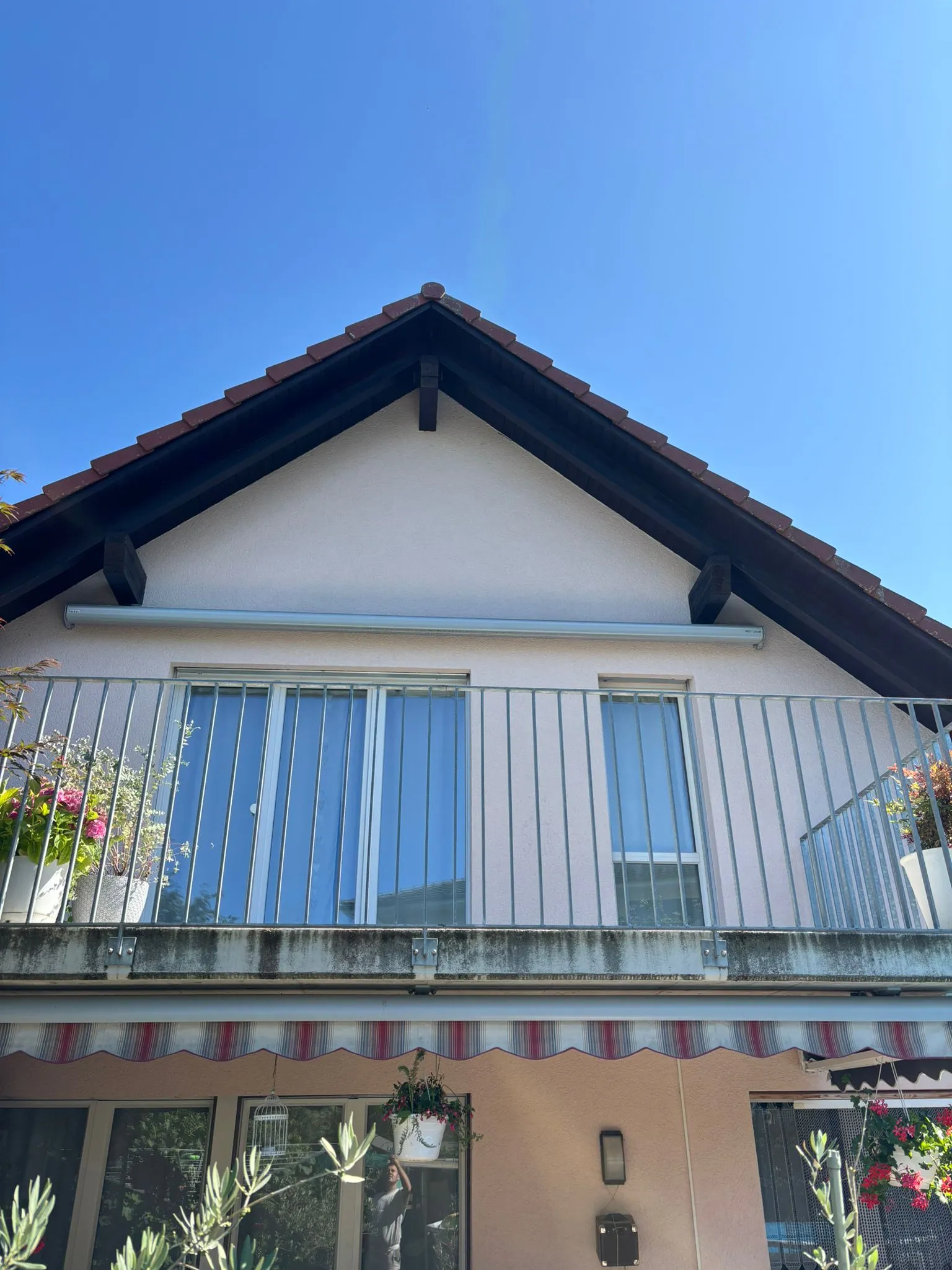 Zweistöckiges Haus mit Balkon, blauer Himmel und Pflanzen in Blumentöpfen.