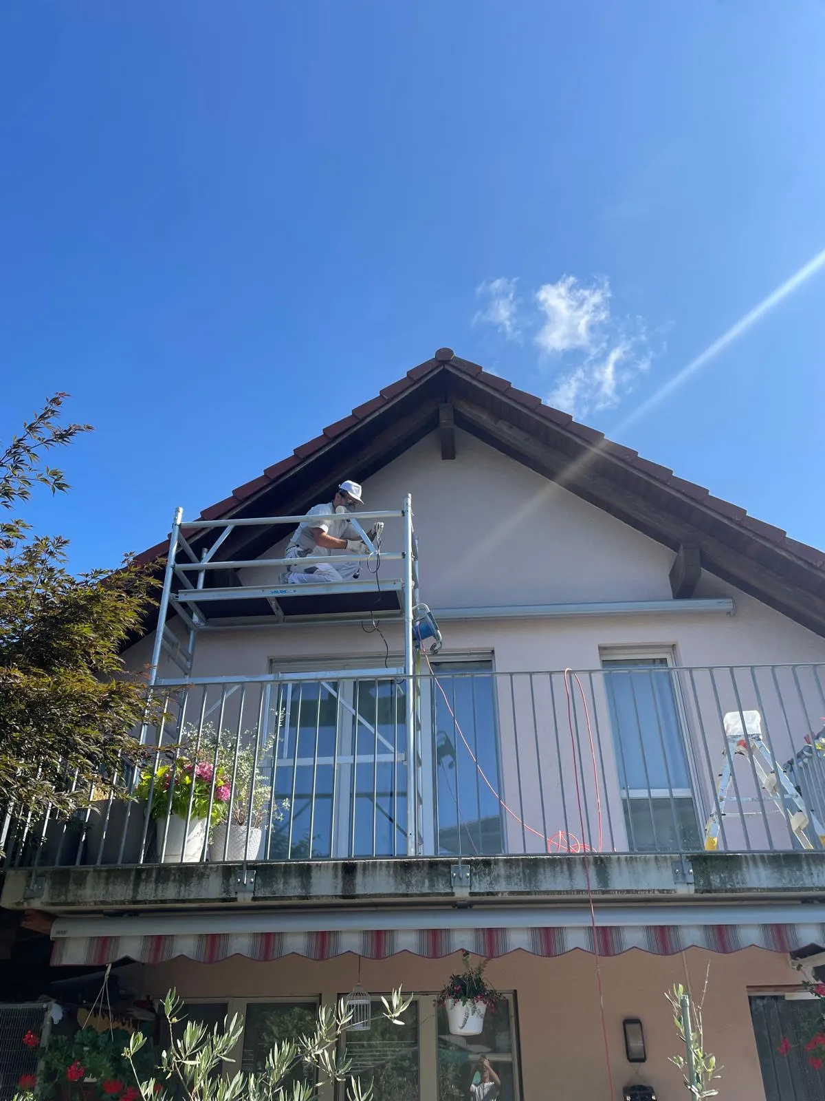 Ein Bauarbeiter auf einem Gerüst arbeitet an der Fassade eines Hauses mit einem blauen Himmel im Hintergrund.