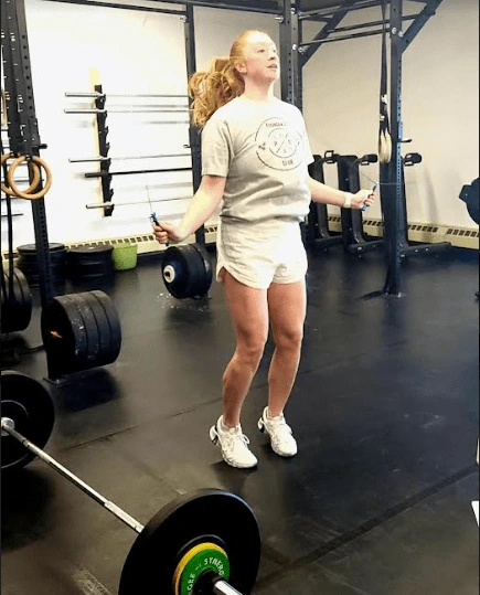 A woman stands in a gym at Iron Prairie Strength Lab in Moosomin, SK, holding a barbell and preparing for a lift.