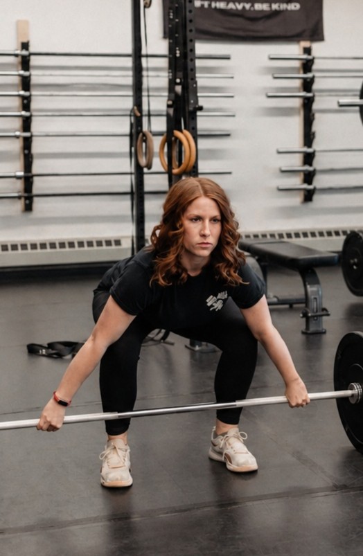 Woman performing a barbell deadlift in a fully equipped gym