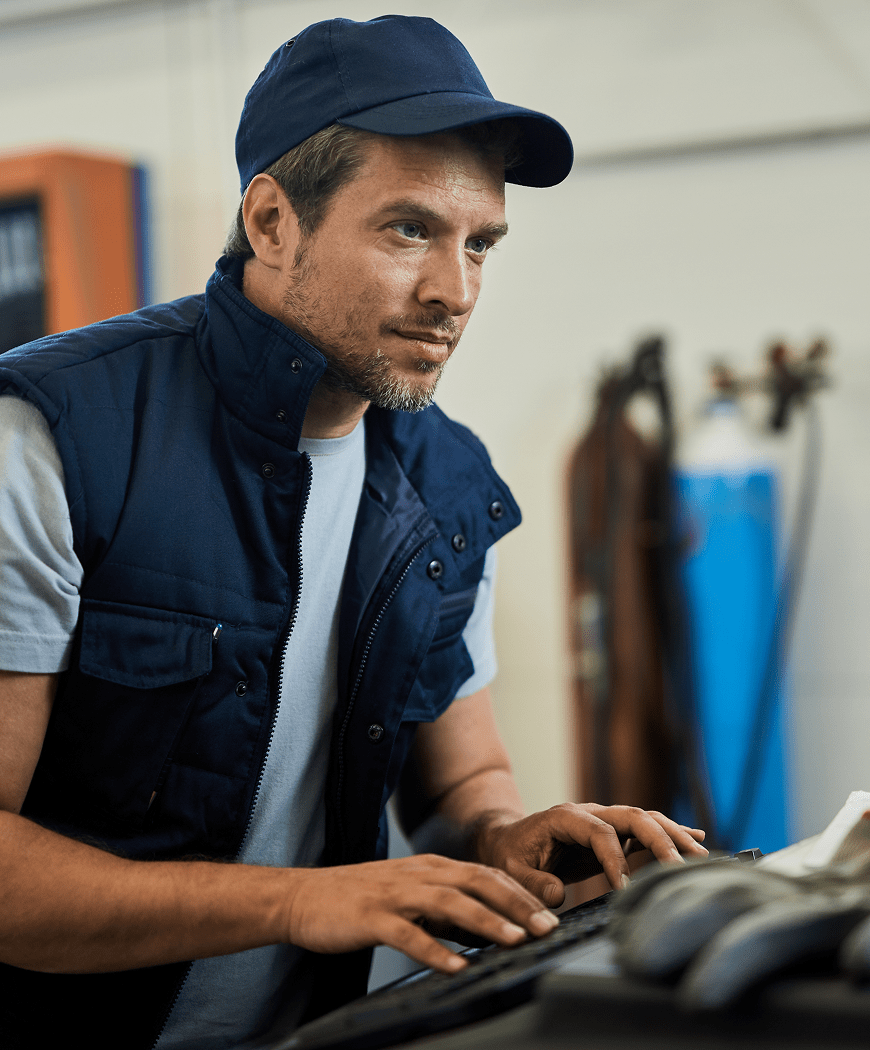 Mechaniker in Arbeitskleidung überprüft konzentriert ein Fahrzeug in der Werkstatt.