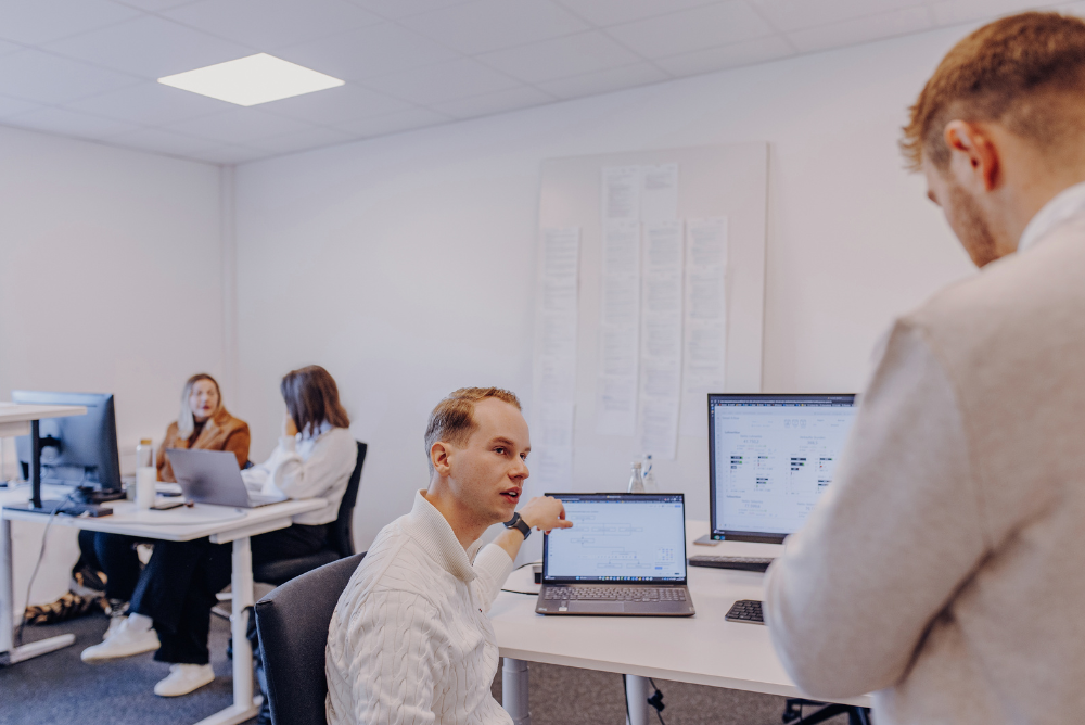 Porträtaufnahme eines lächelnden Mannes im dunkelblauen Polohemd vor dunklem Hintergrund, der ein Tablet in der Hand hält.