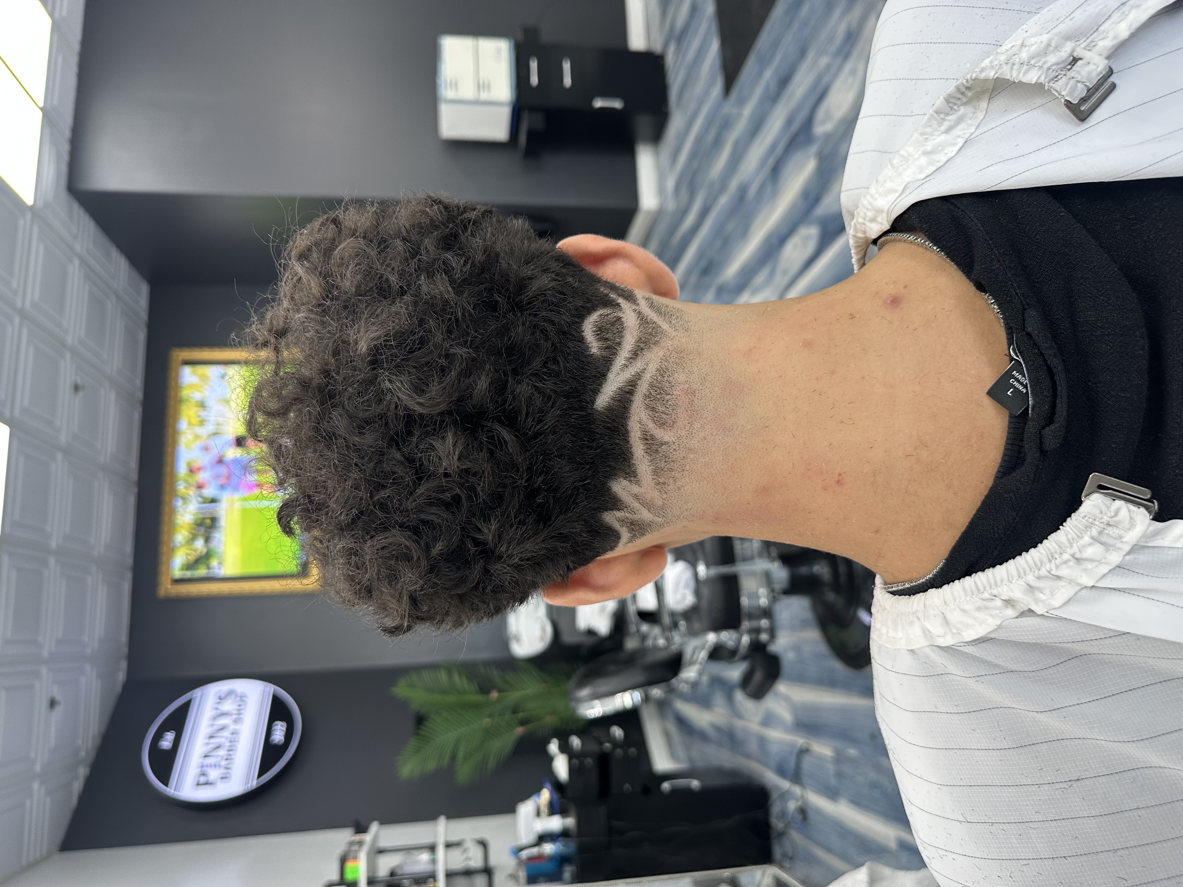 Back of a man's head with curly hair and a fade haircut featuring a wave and circle design.