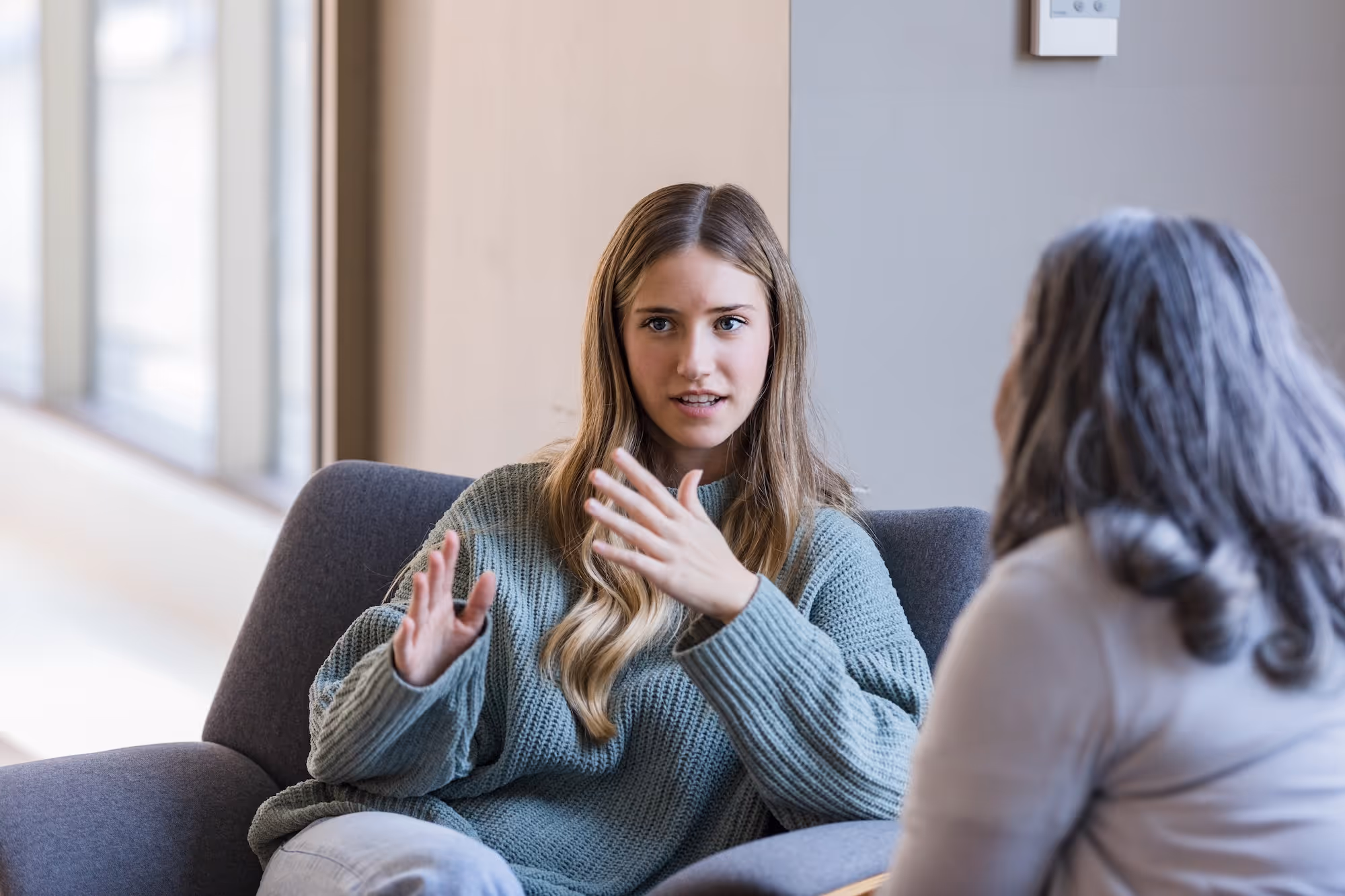 Young woman in a green sweater talking and gesturing with her hands during a conversation.