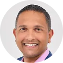 Smiling man with short hair wearing a dark blazer and light shirt against a white background.