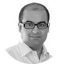 Portrait of a man wearing glasses and a white shirt, smiling slightly, against a white background.