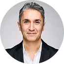 Smiling middle-aged man with gray hair wearing a black blazer and white shirt against a light gray background.