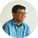 Smiling man with glasses wearing a blue shirt against a plain light background.