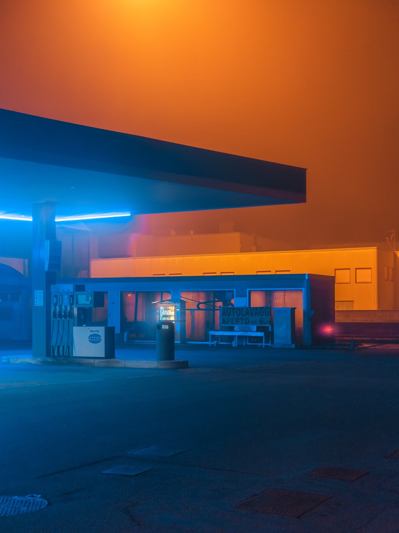 Abandoned gas station illuminated with neon blue and orange lights at night in cinematic urban photography style