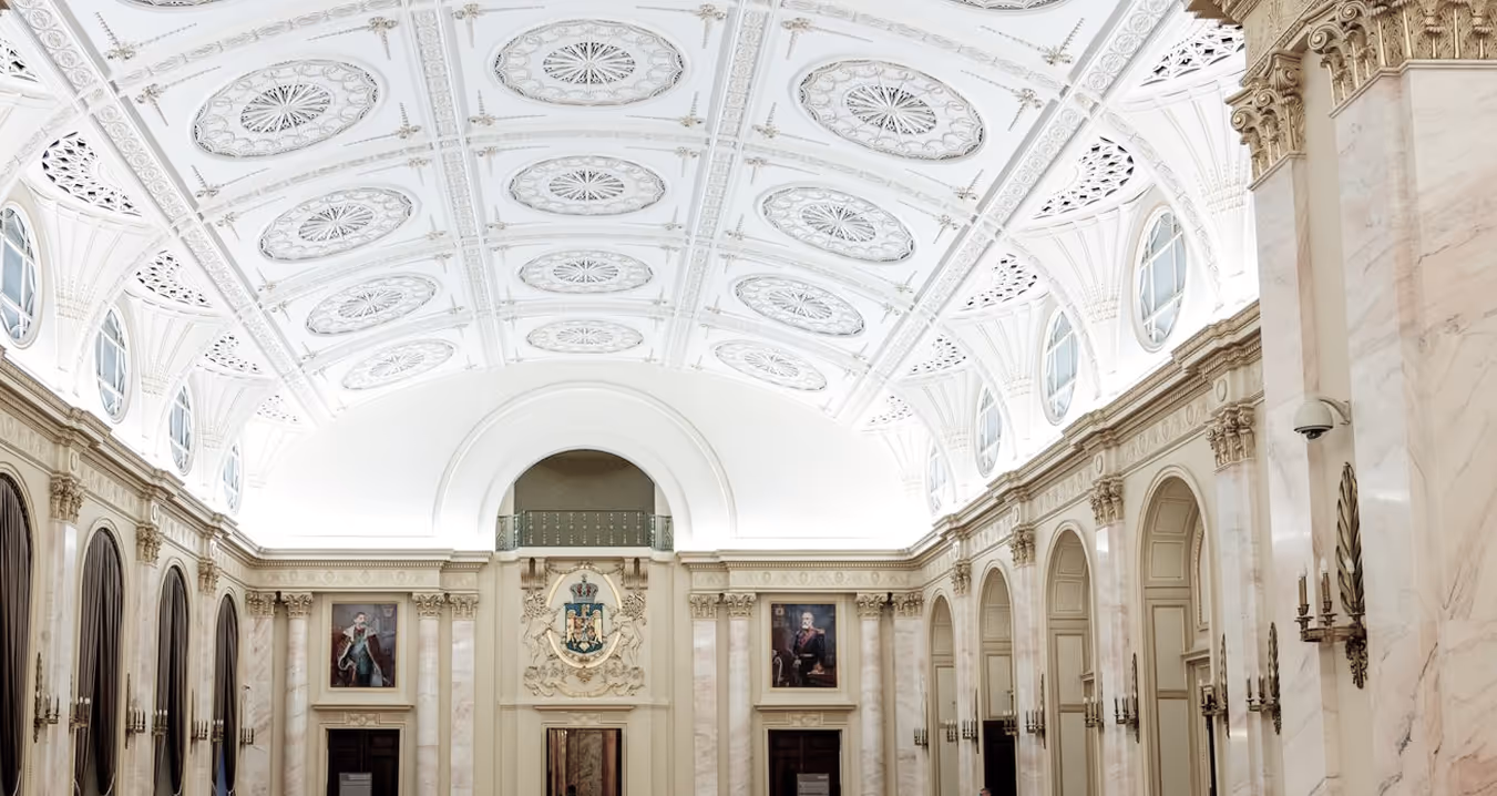 “Spacious neoclassical dining hall with marble columns, vaulted ceiling with ornate plaster medallions, and historic portraits on the walls.”