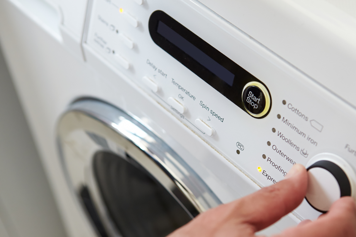 A person adjusting the setting on their washing machine to a more eco-friendly option.