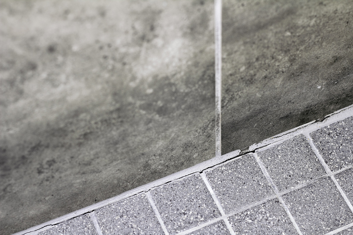 Cracked grout around the floor tiles of a bathroom. These will inevitable allow water to leak through, causing deeper structural damage, rot, and moul growth.