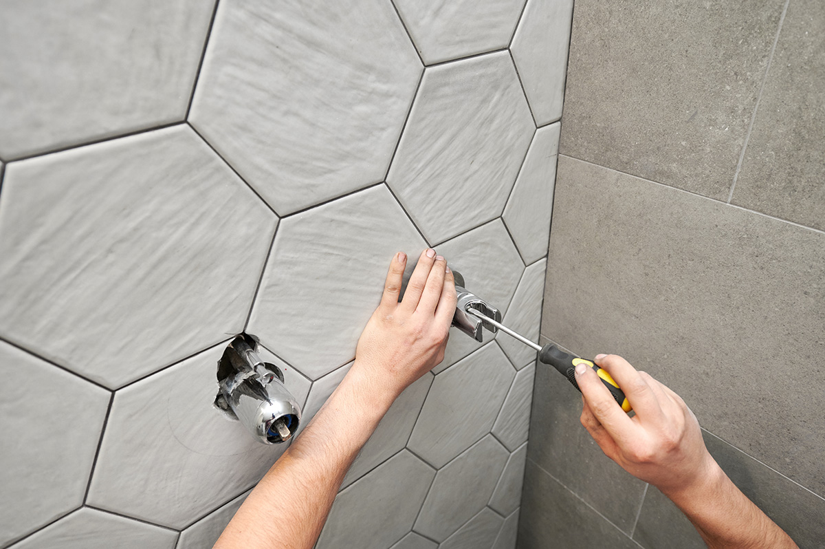 A close-up of a plumber’s hands as he uses a screwdriver to tighten components in a new shower system.