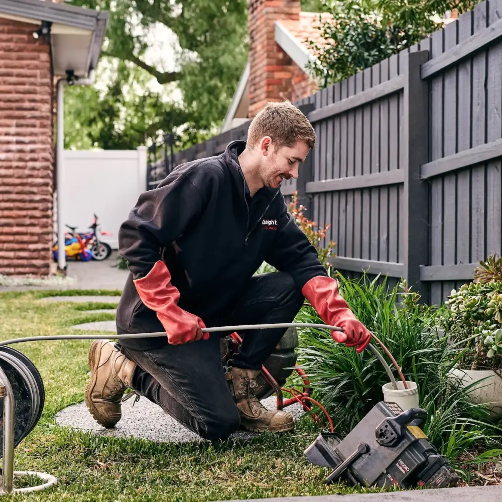 Worker in black jacket and red gloves using plumbing equipment in backyard