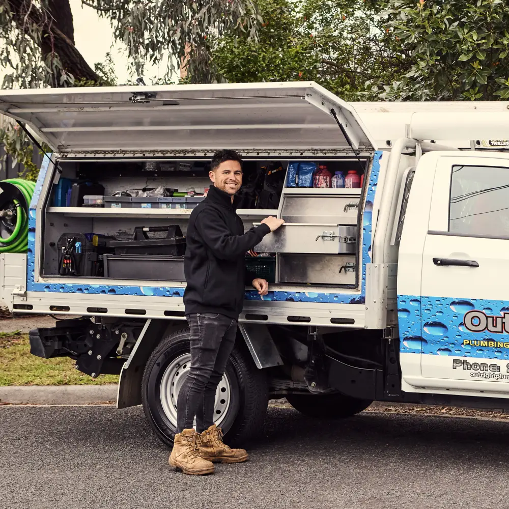 A plumber standing beside a service truck happily preparing to do a plumbing service