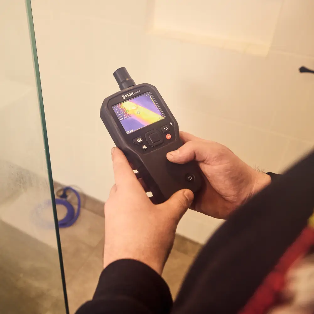 FLIR thermal imaging camera displaying colorful heat map near glass surface