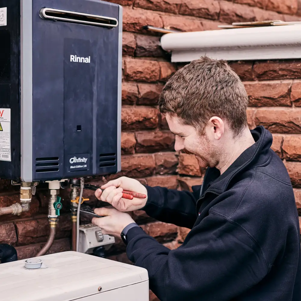 Technician repairing Rinnai water heater against brick wall