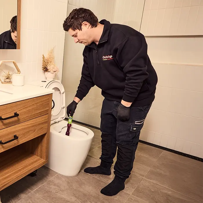 Plumber in black uniform fixing toilet in modern bathroom