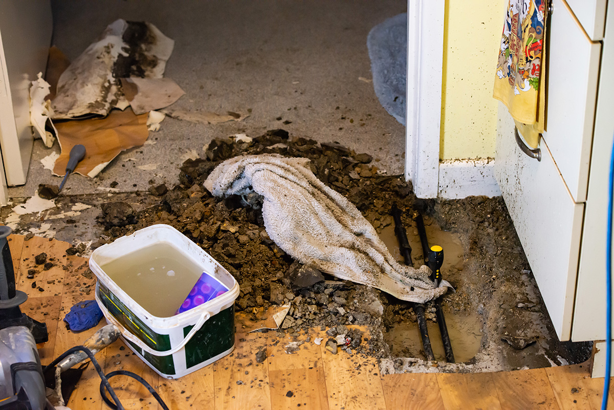 An absolute mess in a Melbourne kitchen, where an amateur plumber has attempted to fix a burst pipe under the floor by digging up the floor themselves. There is dirt, filth and water everywhere.
