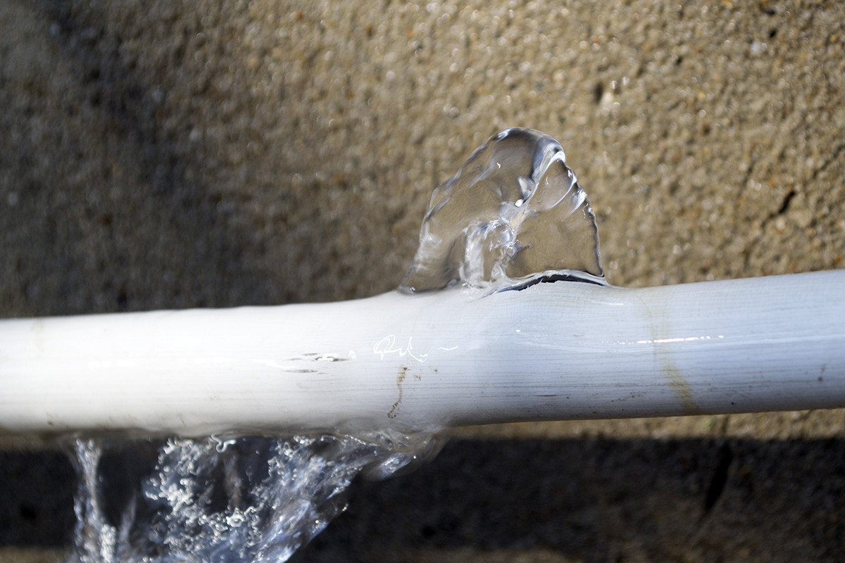 Frozen water bursting through cracked white pipe against textured wall