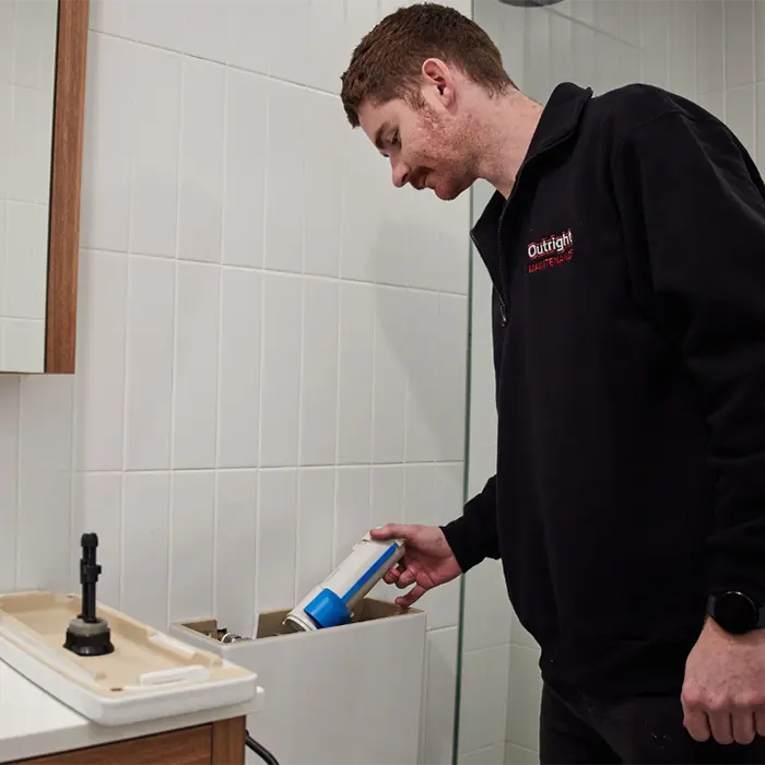Worker in black jacket using cleaning product in tiled bathroom