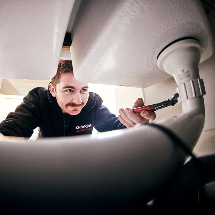 Maintenance worker fixing plumbing under sink with wrench