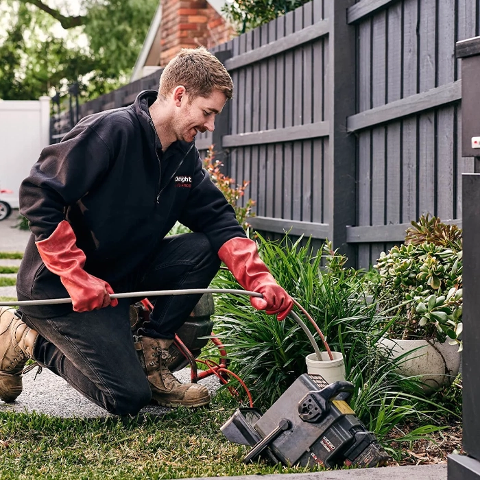 Worker in black jacket using red-gloved hands to operate garden equipment
