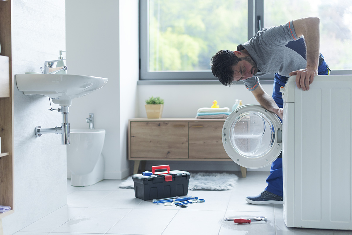 A plumber working on unclogging washing machine.