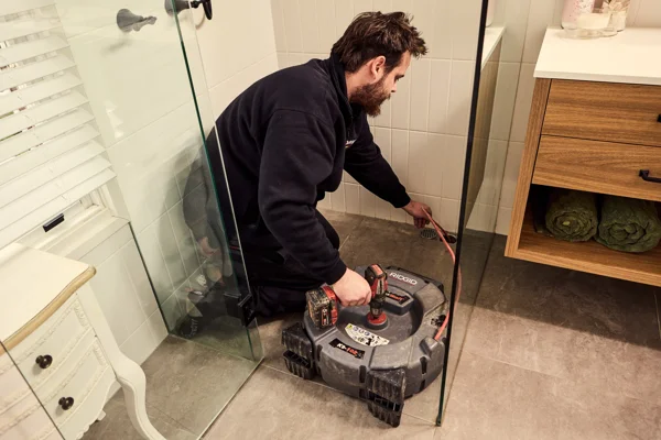 Plumber using flex shaft to unblock shower drain