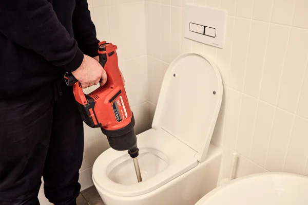 Plumber using a air snake to unblock a toilet during a repair service.