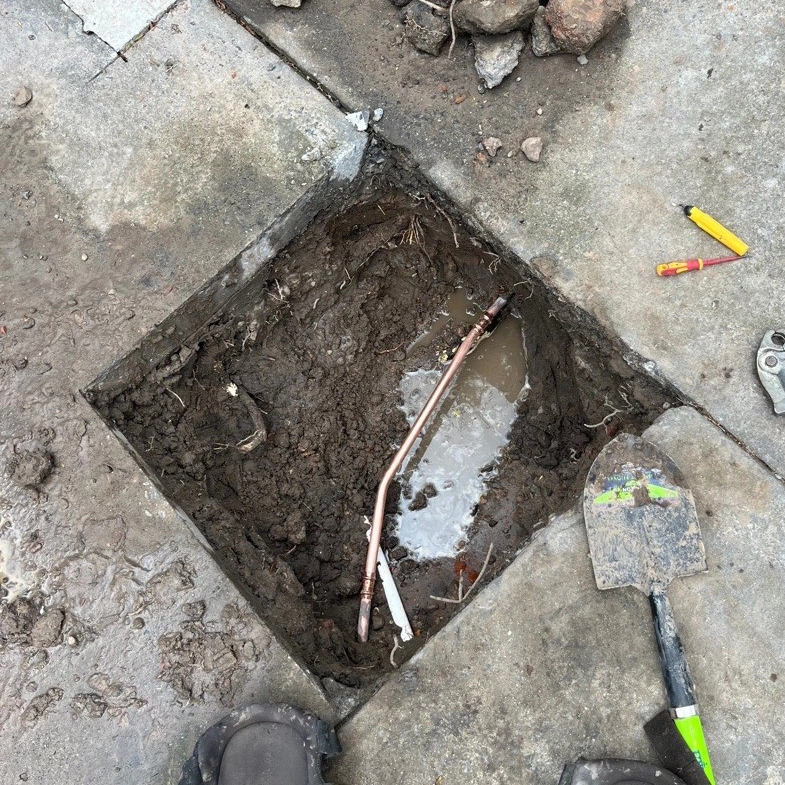 Exposed pipes in a square hole during driveway repair.