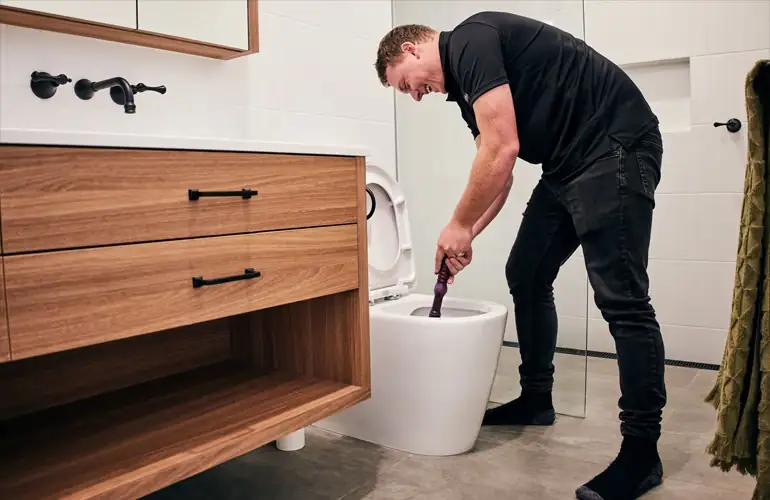 Outright Plumbing staff member working on toilet blockage with plunger