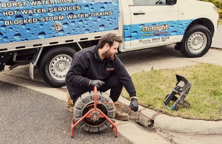 Outright Plumbing plumber with drain camera equipment and cable drum beside a work ute at the kerb