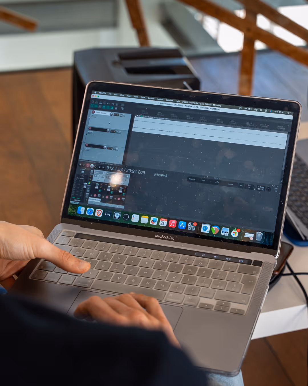 Persona che utilizza un MacBook Pro con un software di produzione audio aperto sullo schermo in un ambiente interno.