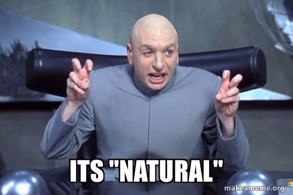 Meme image of a bald man in a gray suit seated in a futuristic chair, making air quotes with both hands. Bold text reads, “ITS ‘NATURAL’.” The image jokes about skepticism toward something being described as natural.