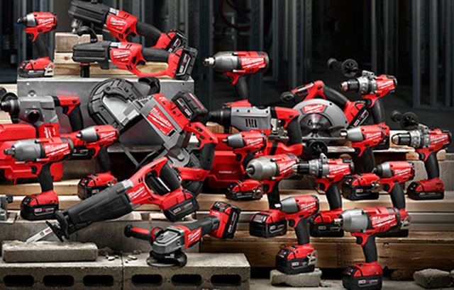Assortment of red and black Milwaukee cordless power tools including drills, saws, and impact drivers arranged on concrete blocks and wooden planks.