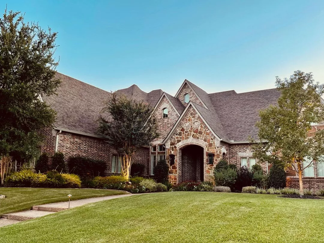 Luxury brick home with steep gable roof during sunset, ideal for illustrating CLC Roofing’s professional roof inspection services.